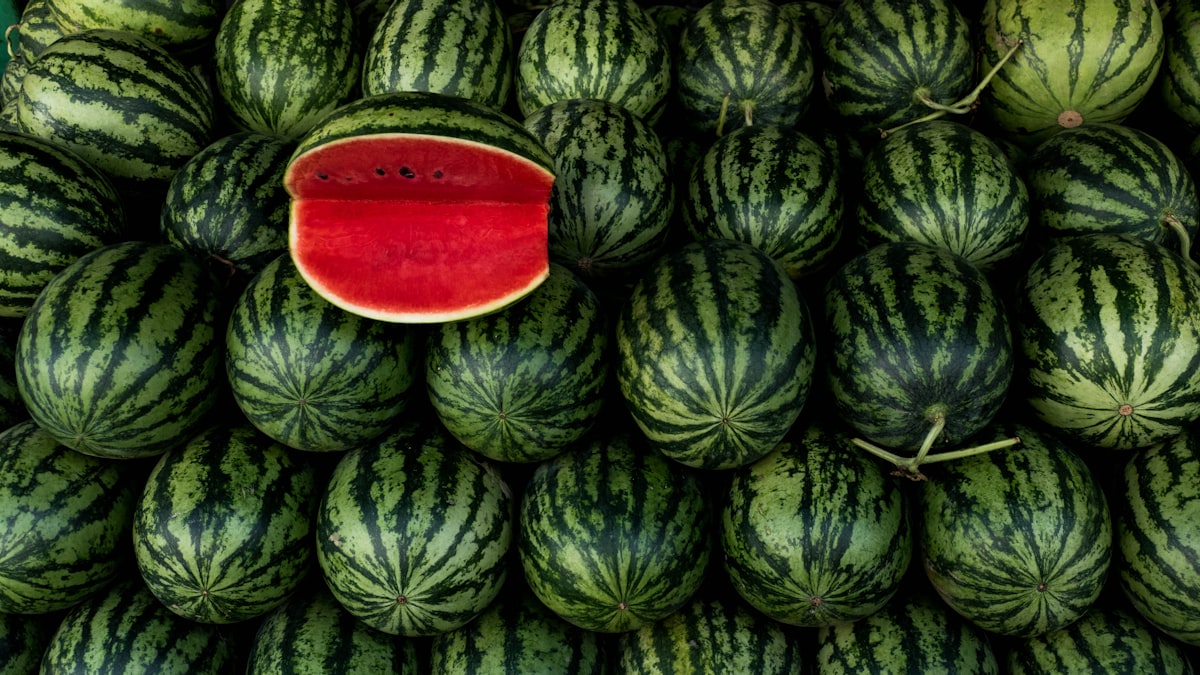 Stacked whole watermelons with one halved to show bright red flesh