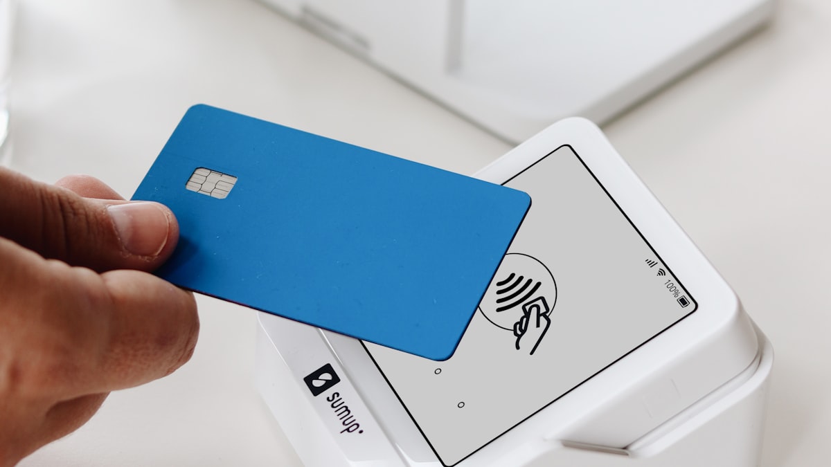Hand holding a plain blue chip card against a white contactless card terminal