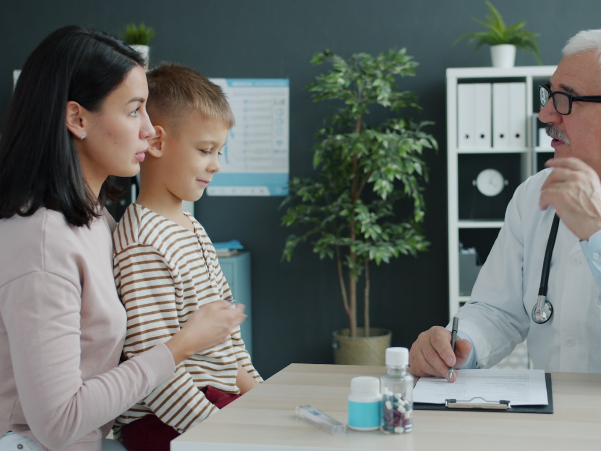 A mother and her son at a clinic desk talking with a doctor during a checkup visit