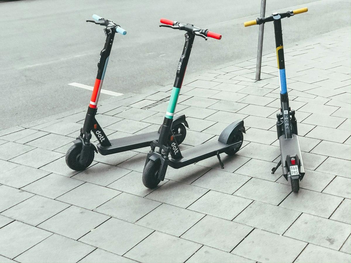 Three shared electric kick scooters parked neatly in a row along a city sidewalk in daytime