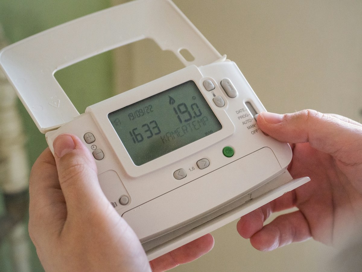 Hands adjusting a wall heating thermostat showing 19.0 degrees Celsius