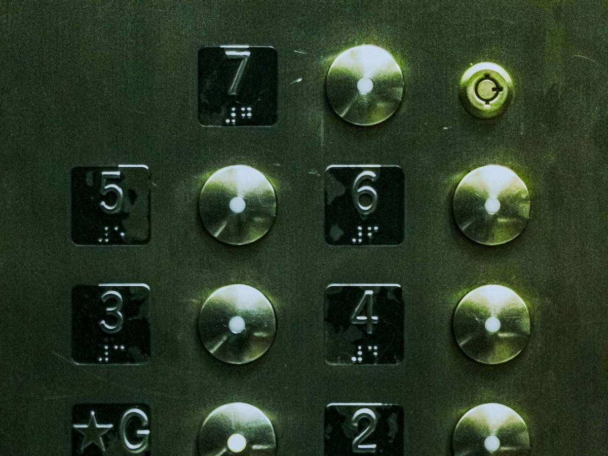 Close-up of a worn, dimly lit elevator button panel with illuminated floor buttons (3 through 7) and braille markings