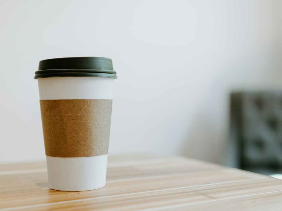 A plain white and brown paper to-go coffee cup sitting on a wooden table