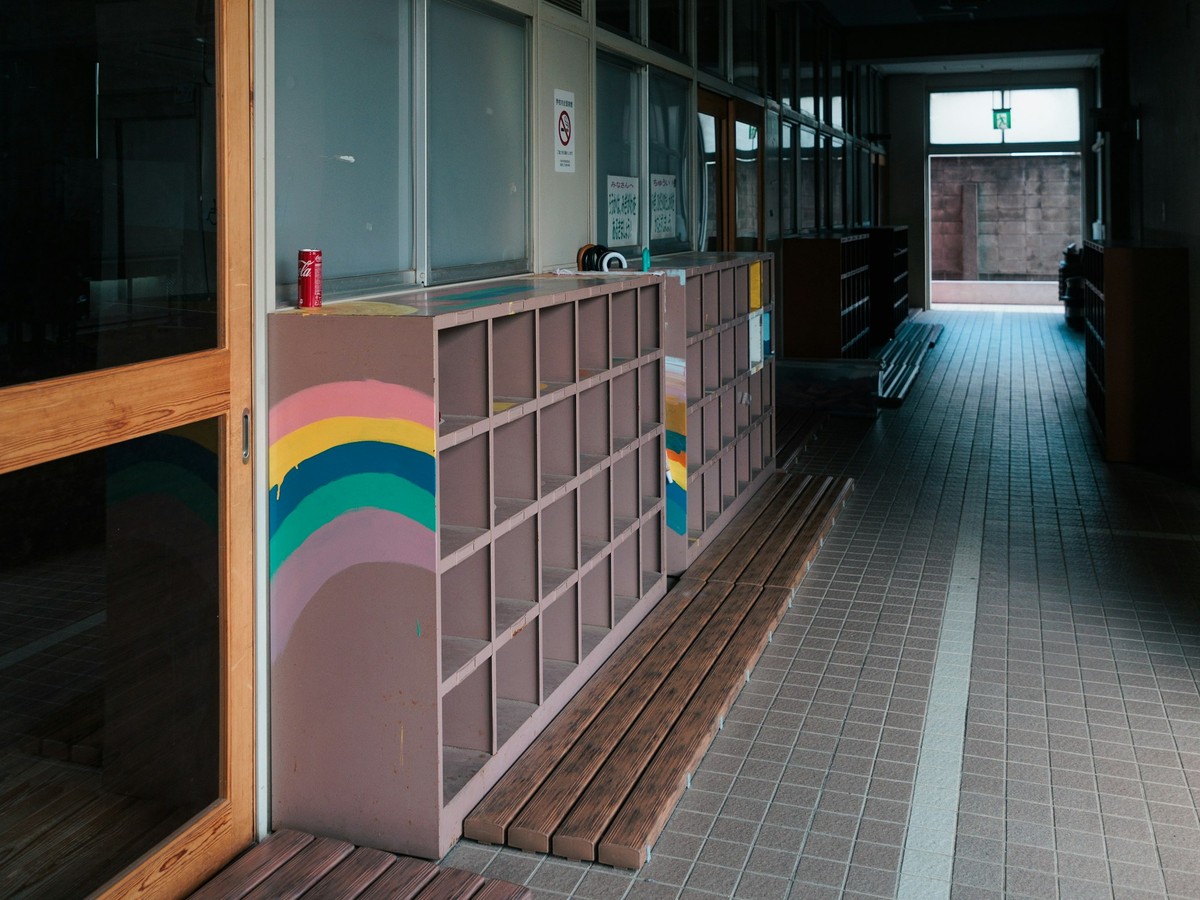 A quiet school hallway with rainbow-painted children's shoe cubbies, a wooden bench and a tiled floor