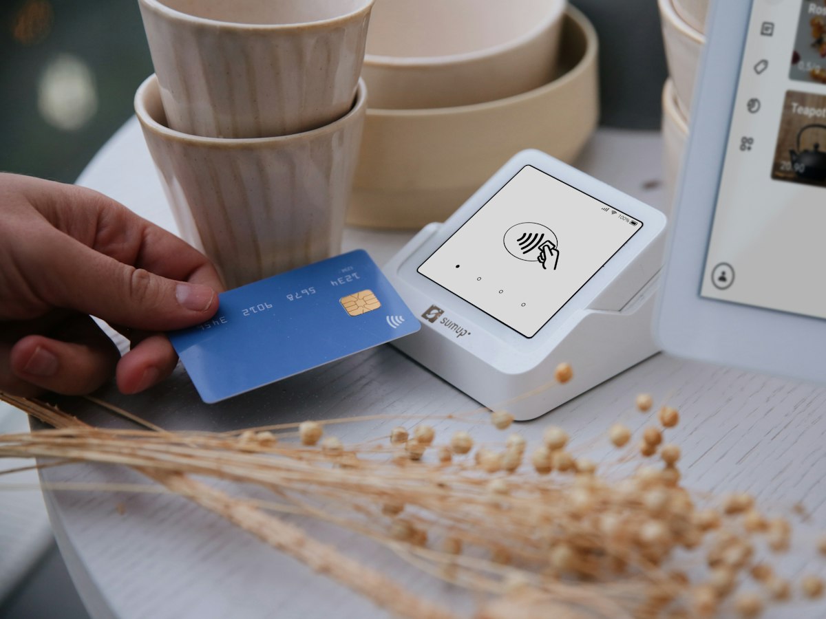 A customer taps a bank card on a wireless payment reader with one hand, paying in seconds with no ceremony