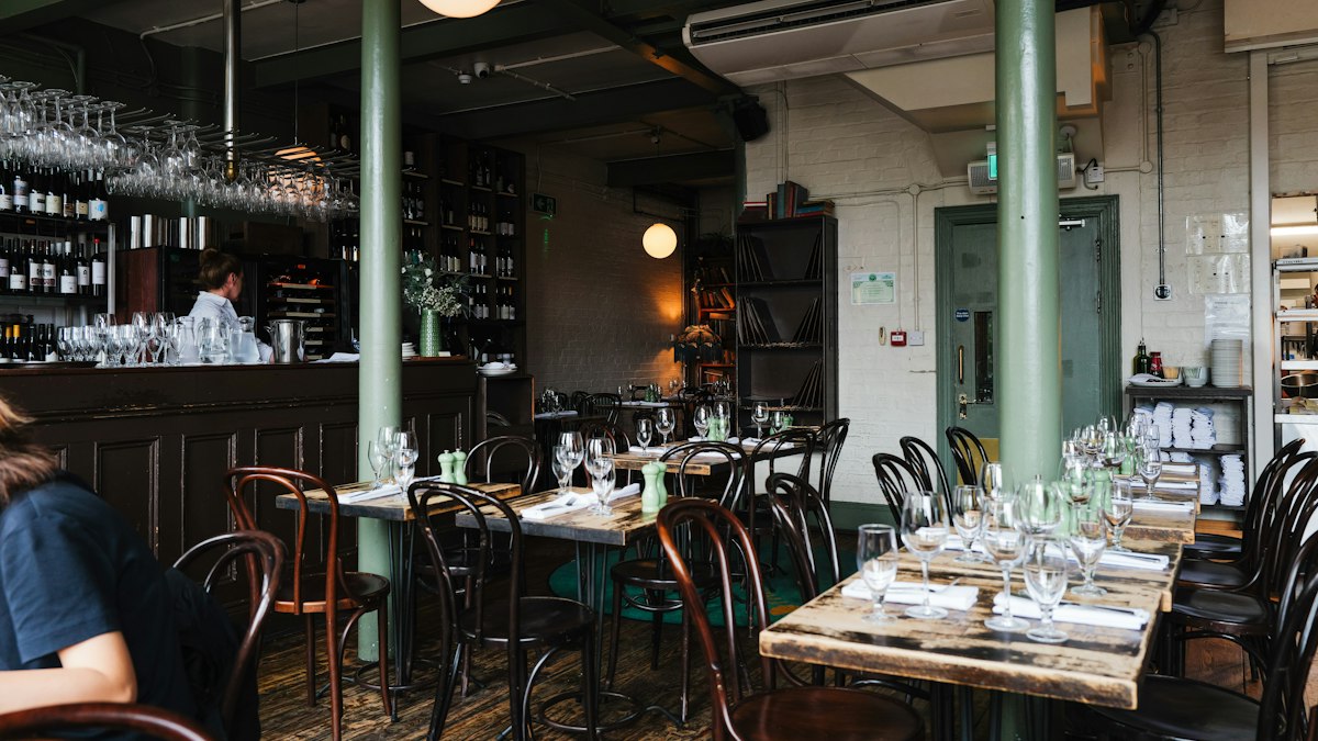 Interior of a wine-bar style restaurant with a bar counter, hanging wine glasses, and reserved dinner tables set with glassware