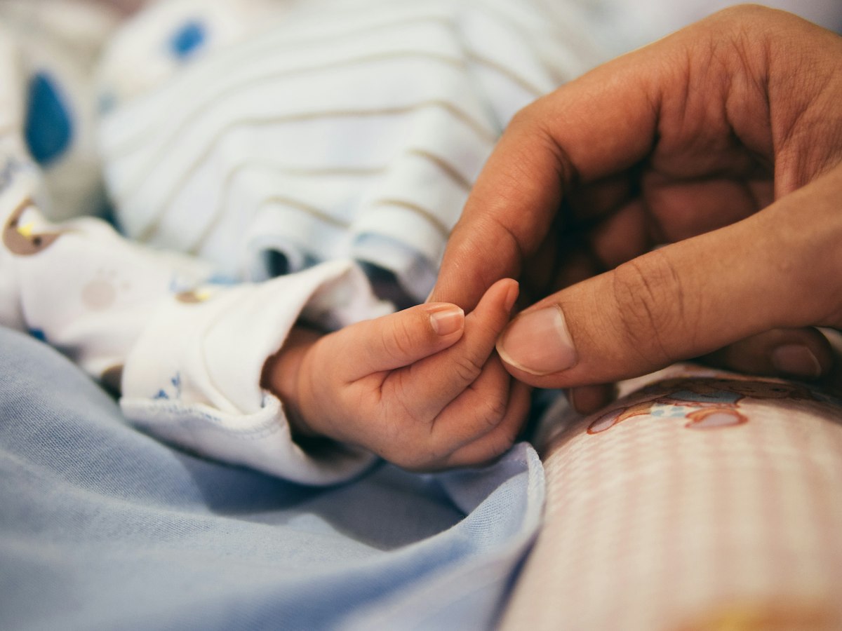 A parent's hand holding a newborn's small hand